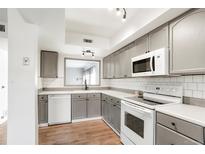 Updated kitchen boasts grey cabinetry, subway tile backsplash, white appliances, and wood-look flooring at 1279 S Sable Blvd, Aurora, CO 80012