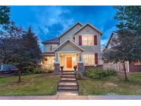 Inviting two-story home with a manicured lawn, orange front door, and charming architectural details at 13053 Umatilla Ct, Denver, CO 80234