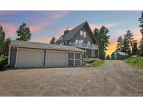 Two-story blue home featuring an attached two-car garage, a small shed, and surrounded by trees at 1472 Sinton Rd, Evergreen, CO 80439