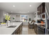 Bright kitchen featuring stainless steel appliances, dark wood cabinetry and island with sink, and view to living area at 4360 S Braun Ct, Morrison, CO 80465