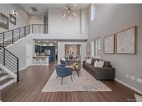 Open-concept living room features high ceilings, modern chandelier, wood floors, and seamless flow to kitchen and dining area at 10523 Ashfield St # 5C, Highlands Ranch, CO 80126