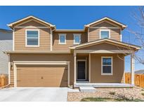 Tan two-story home with a two car garage and covered front porch on a clear day at 261 Mesa Ave, Lochbuie, CO 80603