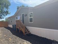 Side view of a home with gray siding and a small wooden porch with steps leading to the front door at 811 Plum N Ave, Lochbuie, CO 80603