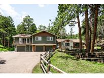 A charming green two-story home features an attached garage and multiple balconies, surrounded by lush trees at 24949 N Mountain Park Dr, Evergreen, CO 80439