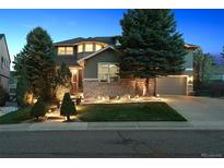 Inviting two-story home with stone accents, lush landscaping, and illuminated front yard at twilight at 8406 Winter Berry Dr, Castle Pines, CO 80108