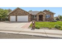 Charming brick home featuring a manicured front yard and a two-car garage with a white door at 1526 Peach Ct, Brighton, CO 80601