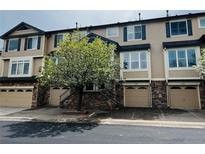 Charming exterior view of townhome with garage, stone accents, blue shutters, and a flowering tree in front at 11328 W Radcliffe Dr, Littleton, CO 80127