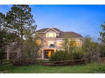 Two-story home featuring a balcony and a partially fenced yard with mature trees and green grass at 7284 Timbercrest Ln, Castle Pines, CO 80108