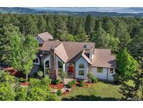 Charming home featuring a red door, stone accents, and a lush green yard with mature trees at 2880 Lake Meadow Dr, Monument, CO 80132