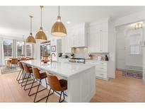 Bright kitchen features white cabinets, island with seating, gold hardware and lighting, and stainless appliances at 15 Latigo Pl, Littleton, CO 80123