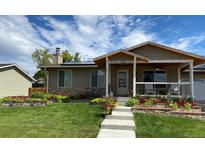 Charming single-story home with a covered porch, stone accents, lush landscaping, and solar panels at 7187 W 79Th Dr, Arvada, CO 80003