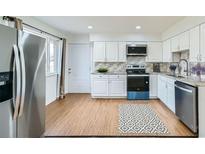 Bright kitchen features stainless steel appliances, white cabinets and a wood floor at 8471 Rainbow Ave, Denver, CO 80229