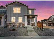 Two-story home boasts stone accents, neutral gray siding, and a welcoming front porch, set against a colorful twilight sky at 259 E 4Th St, Berthoud, CO 80513