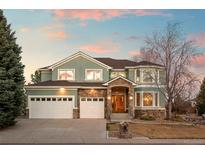 Two-story home featuring a three car garage, green stucco, and stone features at dusk at 1942 Kentmere Dr, Longmont, CO 80504