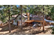 Charming gray home with a stone chimney and a wooden deck nestled amongst tall pine trees at 4835 Abo Ln, Monument, CO 80132