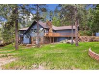 Charming multi-level home featuring a stone chimney and inviting wooden deck surrounded by lush greenery and mature trees at 4835 Abo Ln, Monument, CO 80132