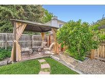 Backyard patio featuring gazebo with curtains, brick flooring, a small fire pit, and manicured lawn at 10223 W 77Th Dr, Arvada, CO 80005