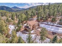 Charming home nestled in the mountains with a deck and beautiful natural landscaping and partial snow cover at 5254 Cheyenne Rd, Indian Hills, CO 80454