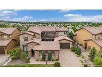 Beautiful tile roof on a tan two-story home with stone accents, a brick driveway, and mountain views in the distance at 9487 Winding Hill Way, Lone Tree, CO 80124