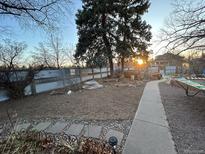 Spacious backyard featuring a well-manicured lawn, garden beds, mature trees, and a modern metal fence at 2602 Jasmine St, Denver, CO 80207