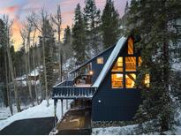 A-frame home with a large deck nestled in a snowy wooded area at dusk at 6365 Highway 9, Breckenridge, CO 80424