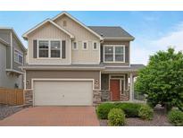 Charming two-story home with a brick driveway, tan siding, stone accents, and a well-manicured front yard at 18173 E 104Th Way, Commerce City, CO 80022