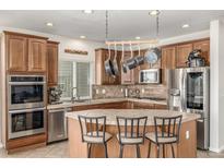 Well-lit kitchen features wood cabinetry, tiled countertops and backsplash, stainless appliances, and a central island with seating at 1335 Galactic Pl, Castle Rock, CO 80108