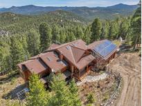 Stunning aerial view of mountain home with solar panels and beautiful surrounding forest at 33121 Lynx Ln, Evergreen, CO 80439