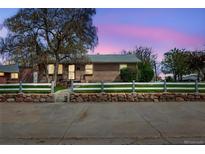 Charming single-story brick home with a white picket fence and stone retaining wall at 6895 E 74Th Ave, Commerce City, CO 80022