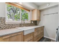 Bright laundry area features a farmhouse sink, mosaic backsplash, gray cabinets, and view to the backyard at 1202 S Troy St, Aurora, CO 80012