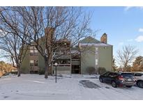 Inviting condo building featuring green siding, a stone chimney, and a snow-covered landscape at 14100 E Temple Dr # W04, Aurora, CO 80015