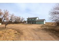 Two-story home featuring a light green exterior with a charming front porch and a spacious unkempt yard at 13654 County Road 13, Longmont, CO 80504