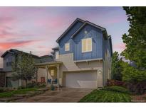 Two-story blue home featuring a two-car garage, covered porch, and manicured lawn at 859 Equinox Dr, Erie, CO 80516