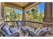 Comfortable covered porch features stone accents, wicker furniture, and views of the surrounding trees at 791 Elk Rest Rd, Evergreen, CO 80439