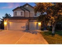 Two-story home featuring brick facade and a three-car garage, set against a twilight sky at 15565 Flowerhill Cir, Parker, CO 80134