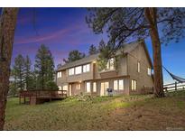 Charming two-story home with a wooden deck, beautiful lawn, and mature trees at dusk at 4992 White House Trl, Evergreen, CO 80439