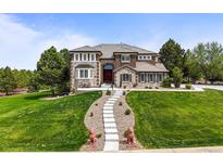 Beautiful front exterior of a multi-story home with a lush lawn, stone accents, and elegant landscaping at 8518 High Ridge, Castle Pines, CO 80108