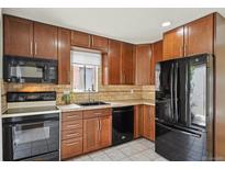 Features a window over the sink, tiled back splash, wood cabinets, and black appliances at 9338 W Utah Pl, Lakewood, CO 80232