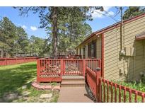 Charming home featuring a wooden deck with red railings, surrounded by green lawn and mature trees at 30400 Hilltop Dr, Evergreen, CO 80439