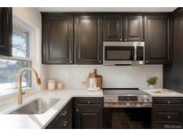 Modern kitchen boasts dark cabinets, stainless steel appliances, white backsplash, and beautiful countertops at 4751 S Xenia St, Denver, CO 80237