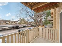 A cozy balcony with wood floors overlooks a parking area and mature trees at 7395 E Quincy Ave # 207, Denver, CO 80237