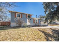 Split level home featuring a blue exterior, brick facade, and a well-maintained front yard with mature trees at 11744 W 71St Pl, Arvada, CO 80004