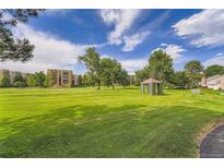 Expansive grassy area with mature trees, gazebo, and residential buildings under a bright sky at 14001 E Marina Dr # 211, Aurora, CO 80014