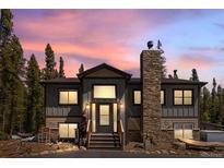 Charming gray exterior home featuring a stone chimney and inviting front porch at dusk at 400 Upper Forest Rd, Idaho Springs, CO 80452
