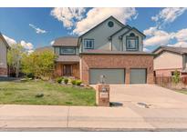 Two story home with brick facade, green siding, a three car garage and a well manicured lawn at 16652 W Archer Ave, Golden, CO 80401
