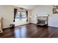Open living room features a brick fireplace, large windows, and hardwood floors at 12425 Bellaire Dr, Thornton, CO 80241