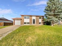 Traditional brick home featuring an attached garage, well-manicured lawn, and mature trees at 12238 Monroe Dr, Thornton, CO 80241