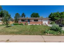 Charming single-story home with a well-manicured lawn, beautiful flowerbeds, and a brick facade at 6043 S Cody Way, Littleton, CO 80123