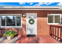 Charming brick home featuring a bright white front door adorned with a wreath and a welcoming 'hello' mat at 6506 Lee St, Arvada, CO 80004