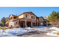 Tan and stone three-story townhouse with three-car garage and snowy landscape at 9876 W Freiburg Dr # G, Littleton, CO 80127